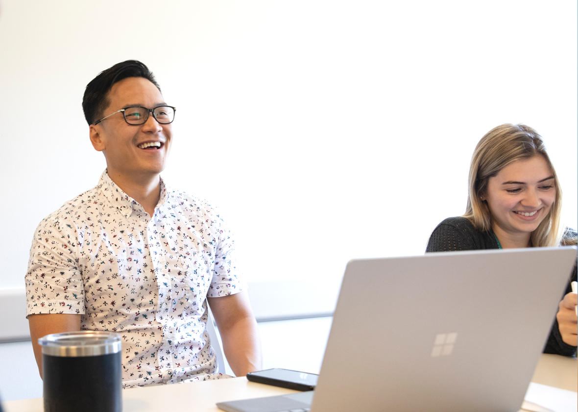 A man and a woman sitting at a conference table laughing