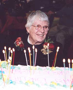 photo taken at a party - marjorie smiles over a cake with lots of candles and wears a corsage of roses