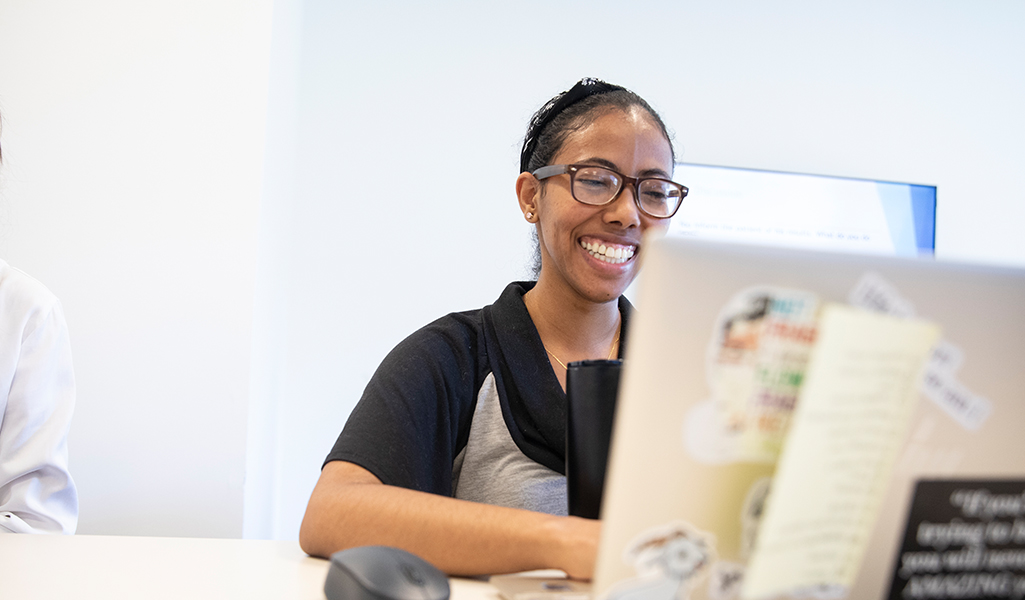 woman smiles and looks at her laptop which is covered with stickers