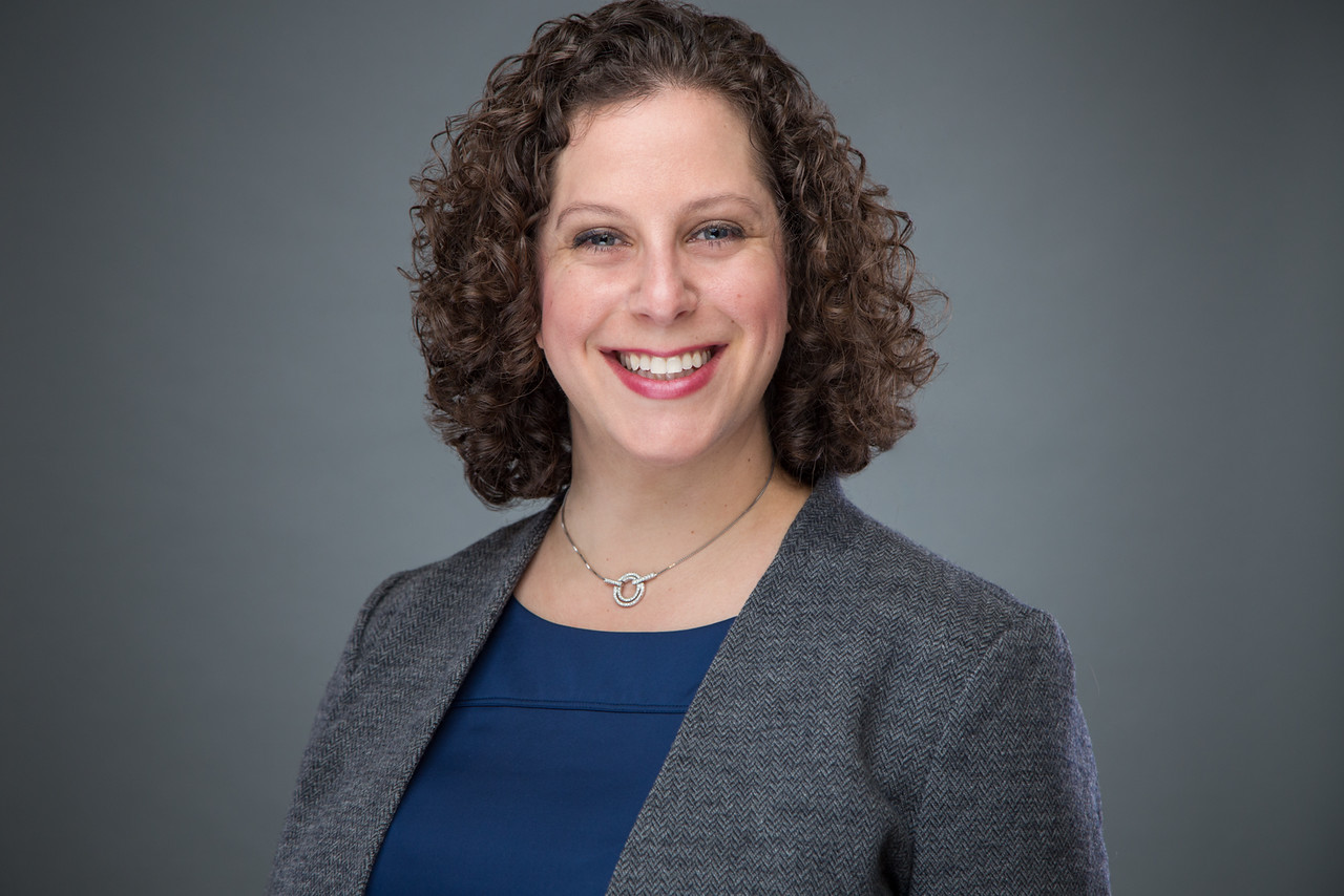 rachel has curly brown hair and wears a grey blazer