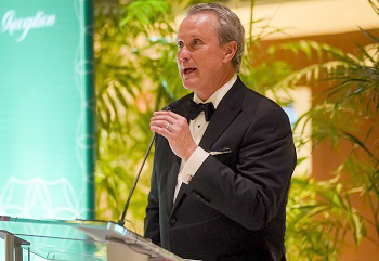 man in tuxedo stands at clear acrylic podium with fancy back lighting and plants
