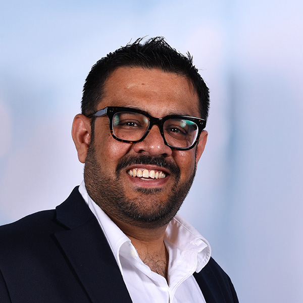 Dev wears a white collared shirt and black rimmed glasses