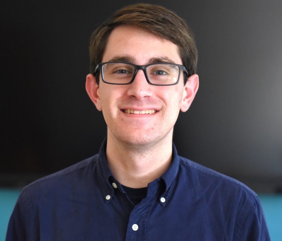 jeremy wears a navy button up and has black rectangular glasses
