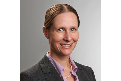 isabel has hair pulled back parted in the middle and wears a purple collared shirt under a grey blazer