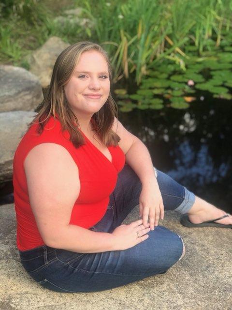 Lauren Talbourdet in red, short sleeved shirt and blue jeans. Lauren has shoulder-length, straight blonde hair.
