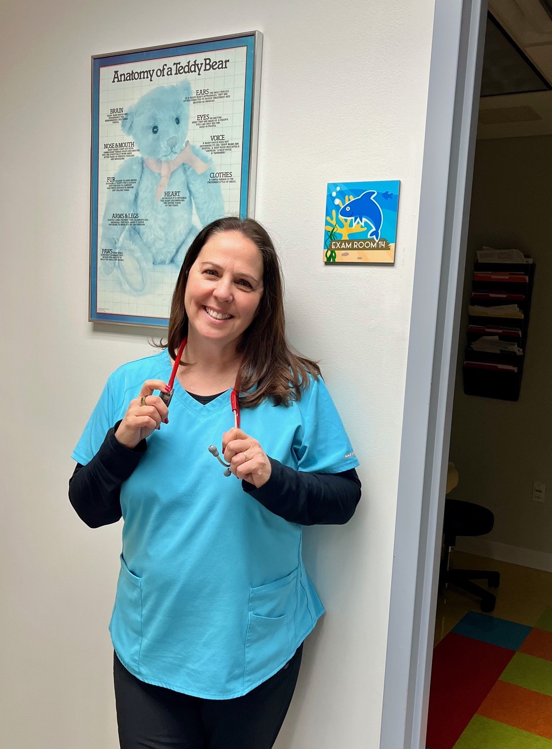woman in blue scrubs with stethoscope around neck and big smile