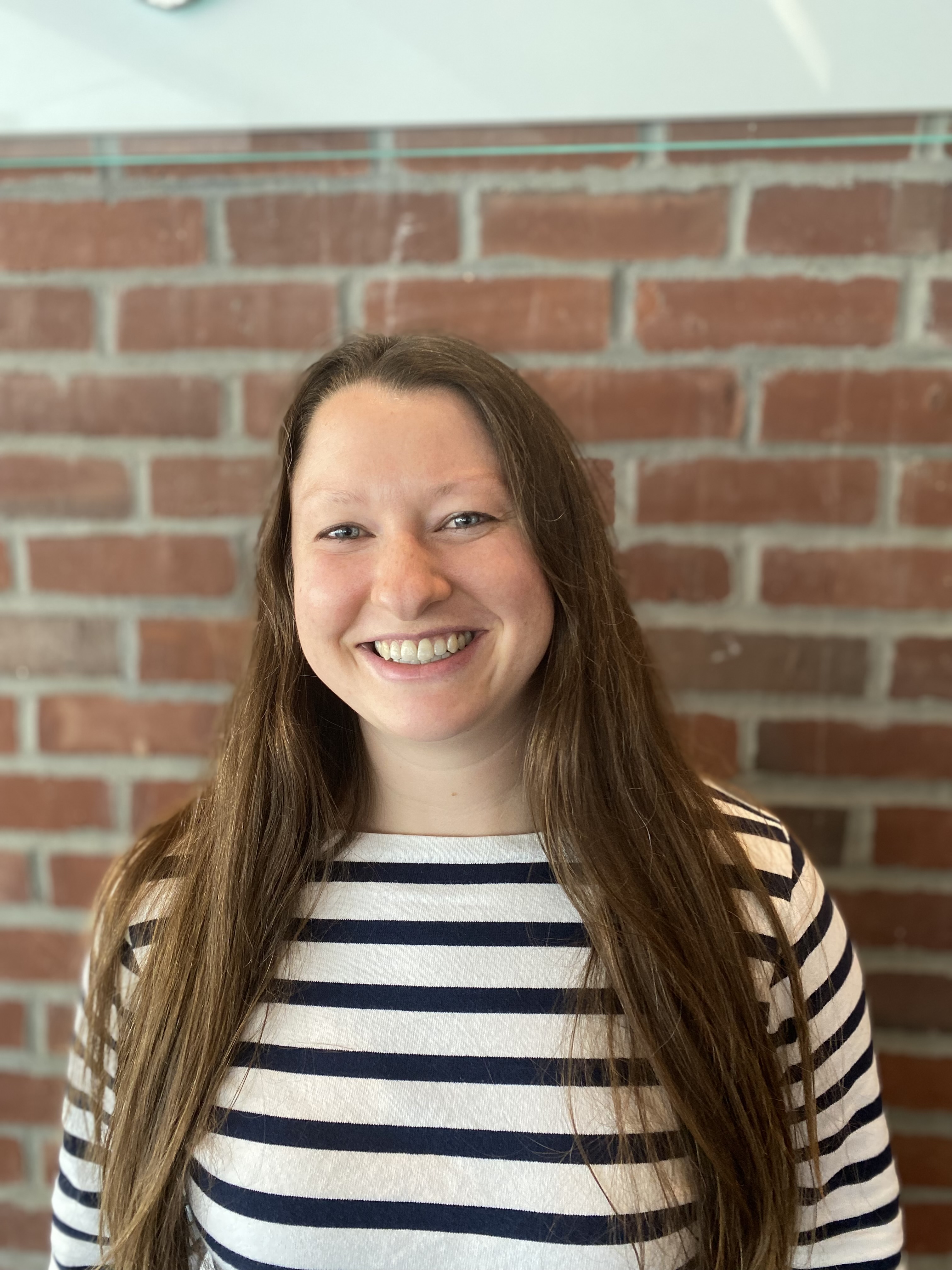 Lindsay McCabe has long brown hair is is wearing a black and white striped shirt.