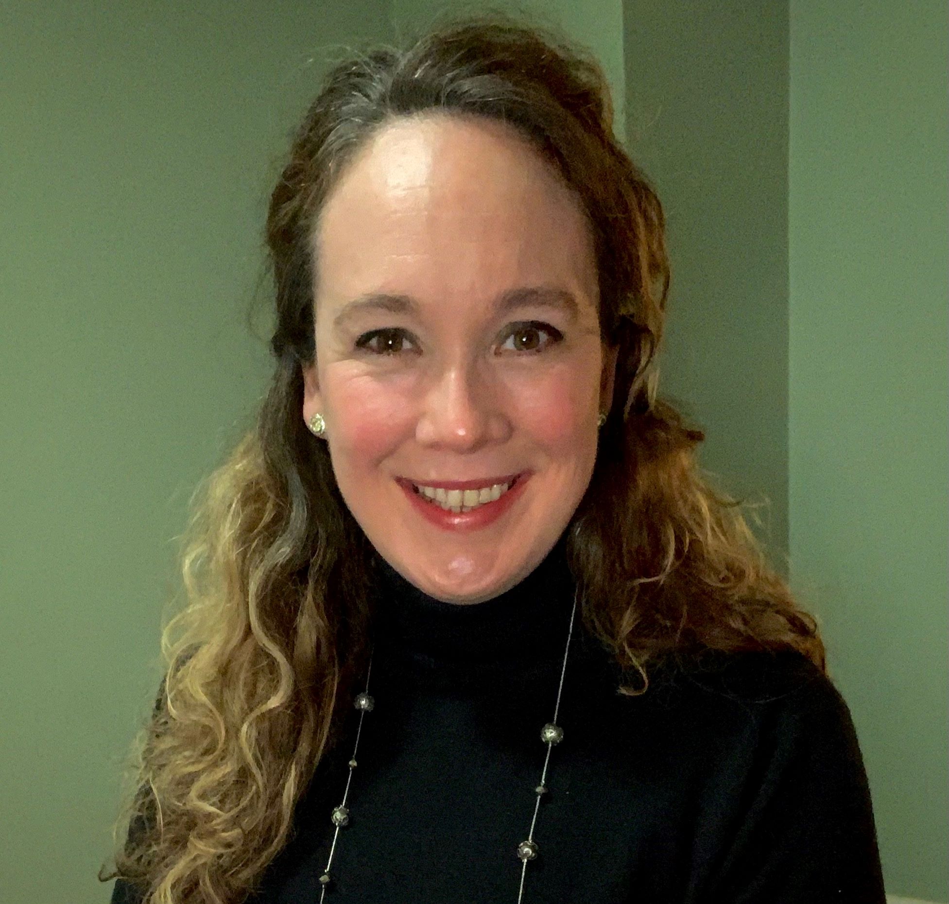 Meaghan Costello has curly, long hair and is wearing a black turtleneck