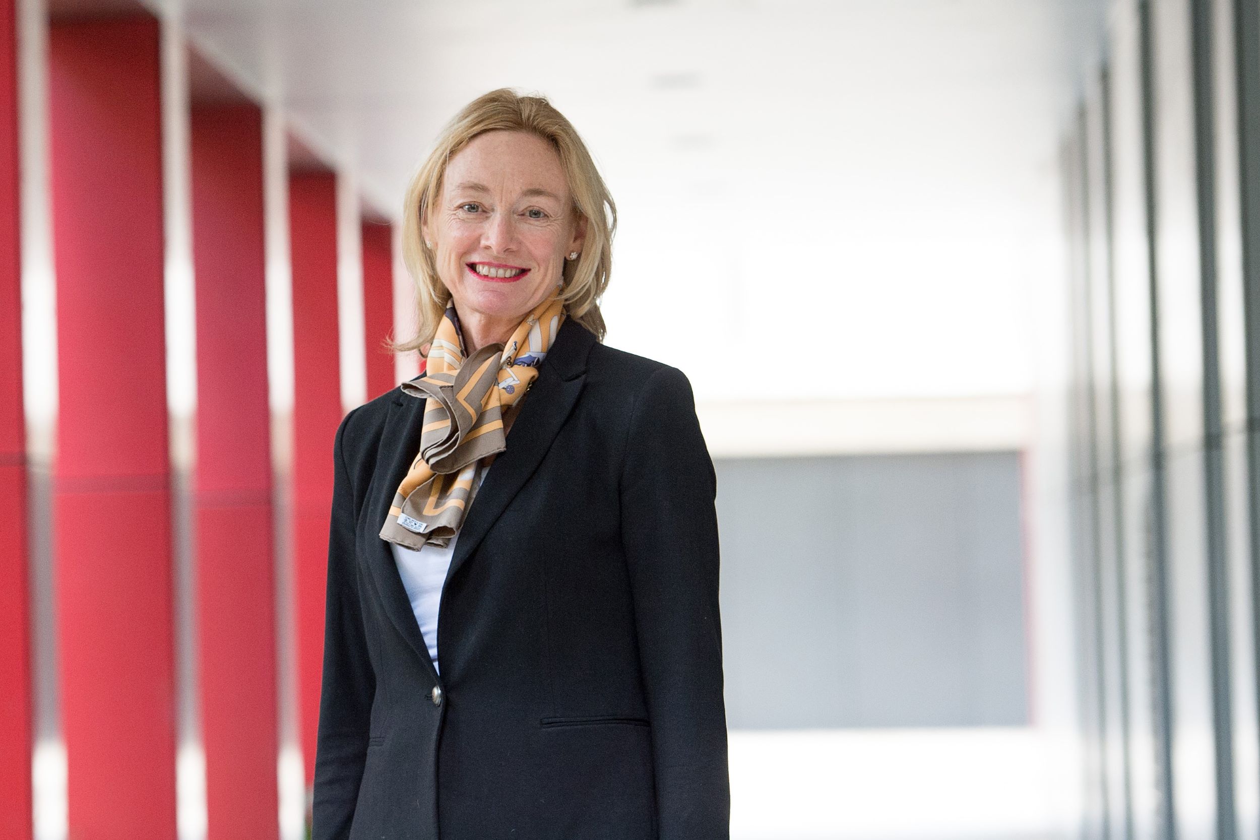 Debra Nestel has shoulder-length blonde hair and is wearing a black blazer and patterned scarf