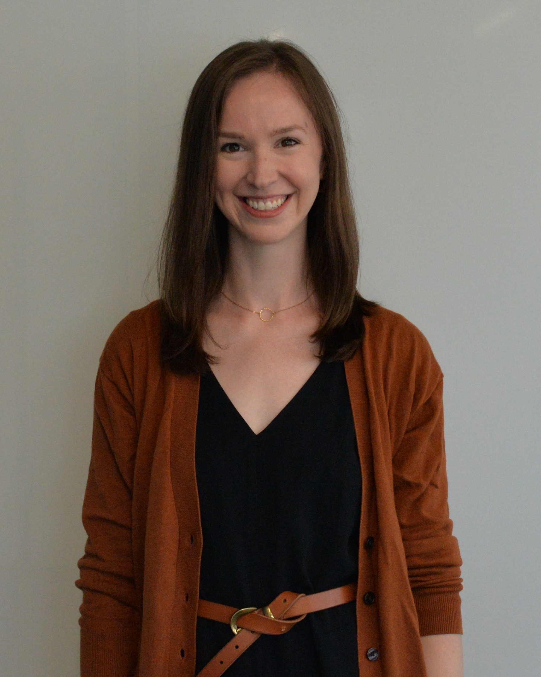 Eileen Gillan has medium brown hair and is wearing a black v-neck dress, and a orange cardigan