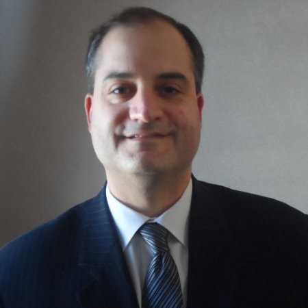Gregory Hamann in a dark suit and white dress shirt with a striped tie.