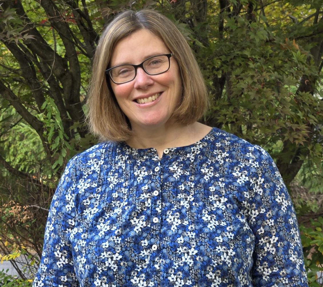 Susan Arruda has a short brown bob, glasses, and is wearing a blue floral shirt