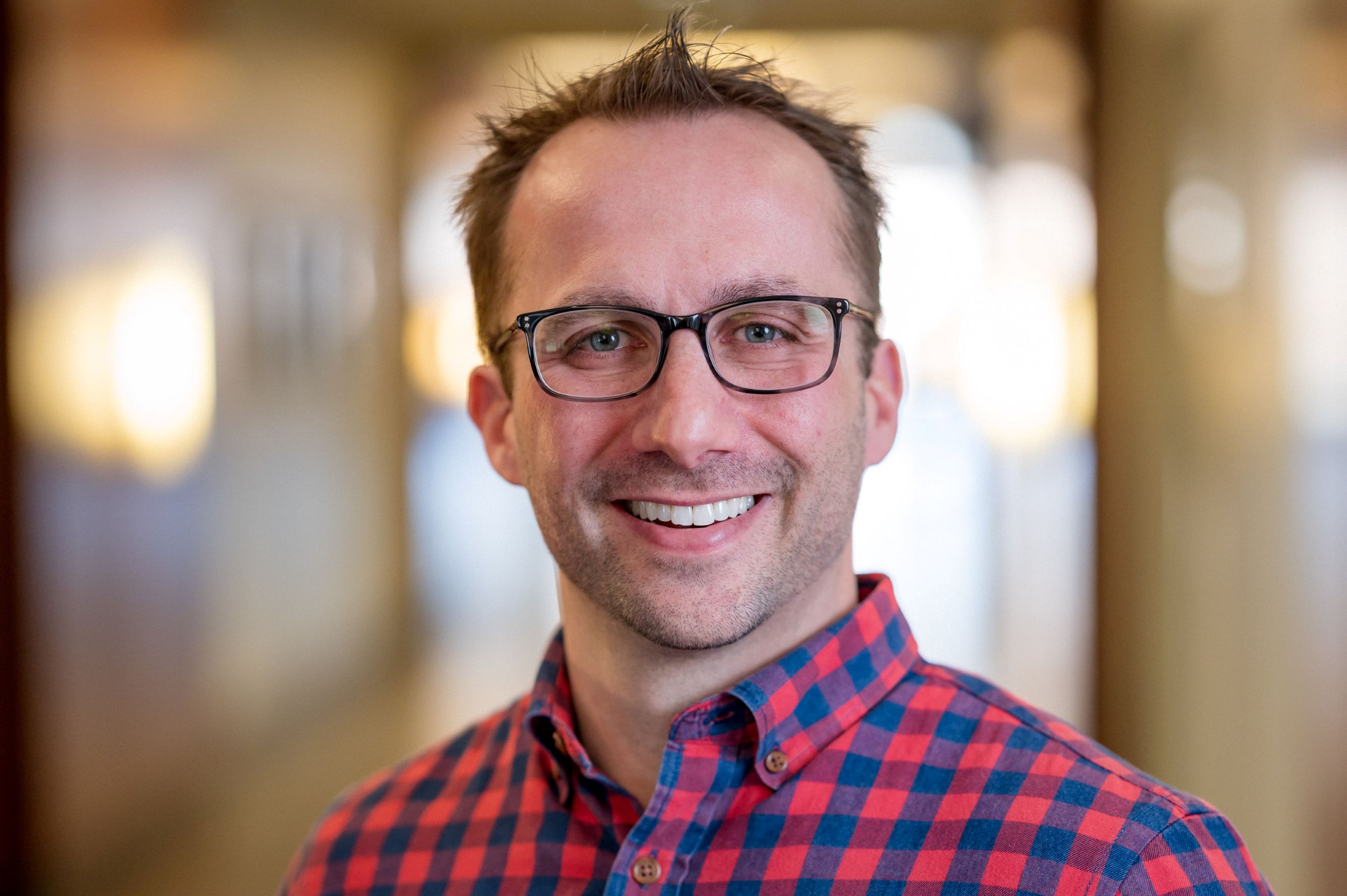 Christopher Joyce has short hair, is wearing glasses, and a red and blue checkered shirt
