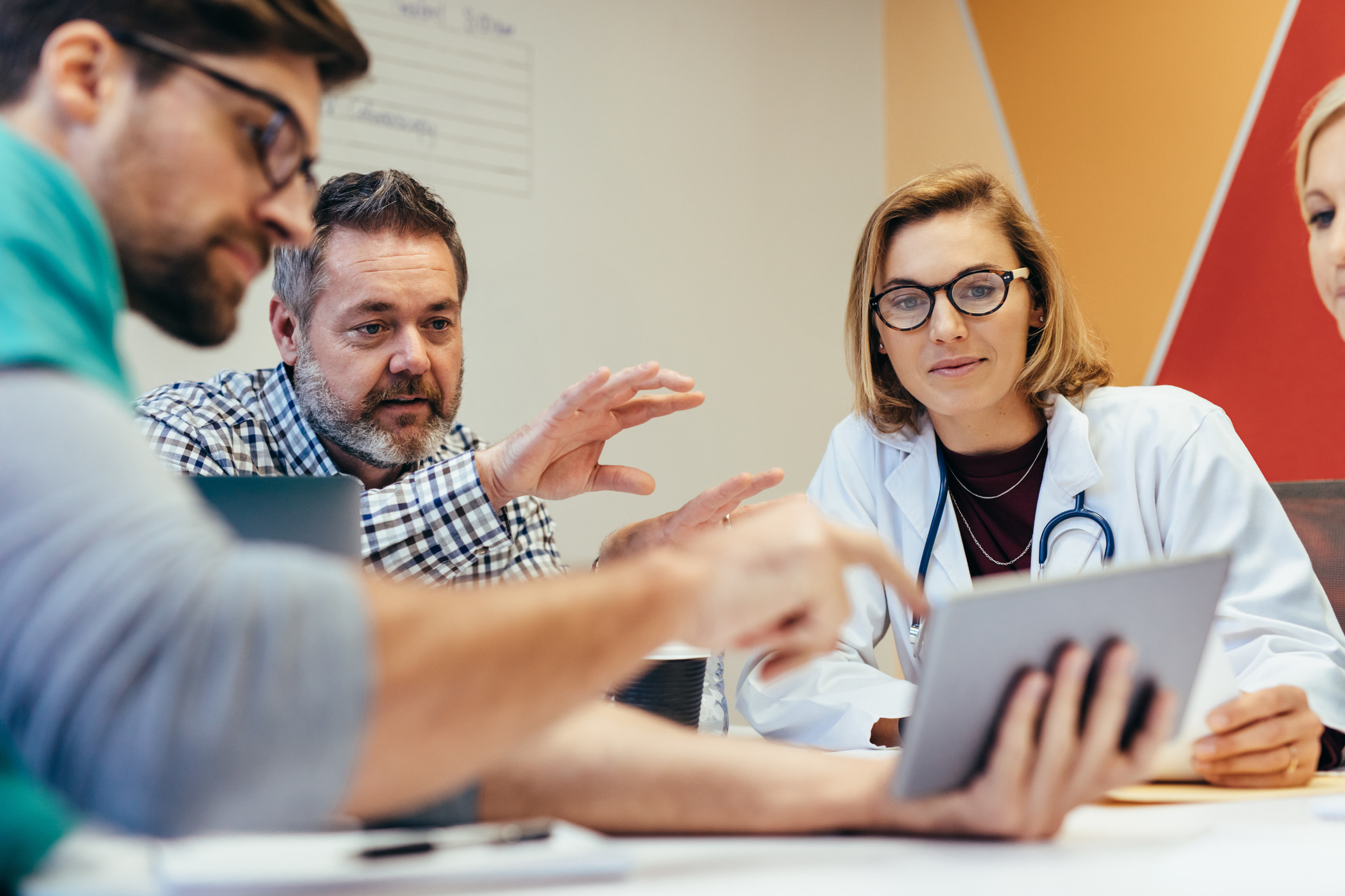 meeting where a bearded man in a business shirt points out something on an ipad to a woman in a lab coat