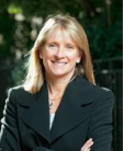 Headshot of woman with long blonde hair smiling and looking at the camera, and wearing a black jacket