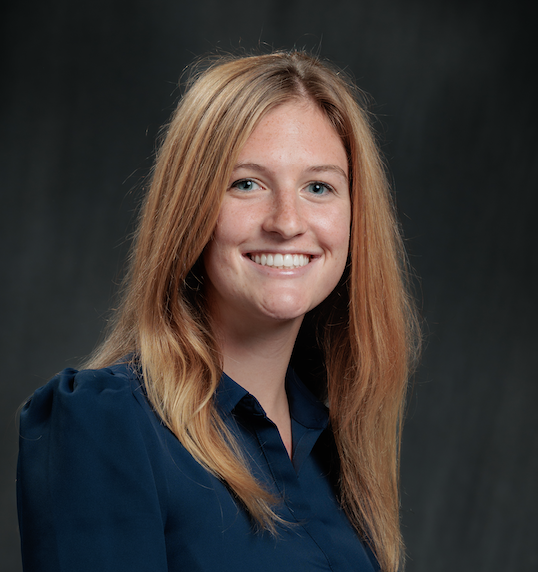 Woman with long blonde hair wearing a blue collared shirt in front of a black background