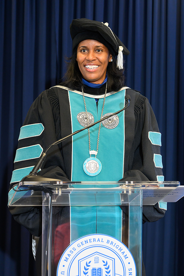 woman in regalia speaks at a clear podium