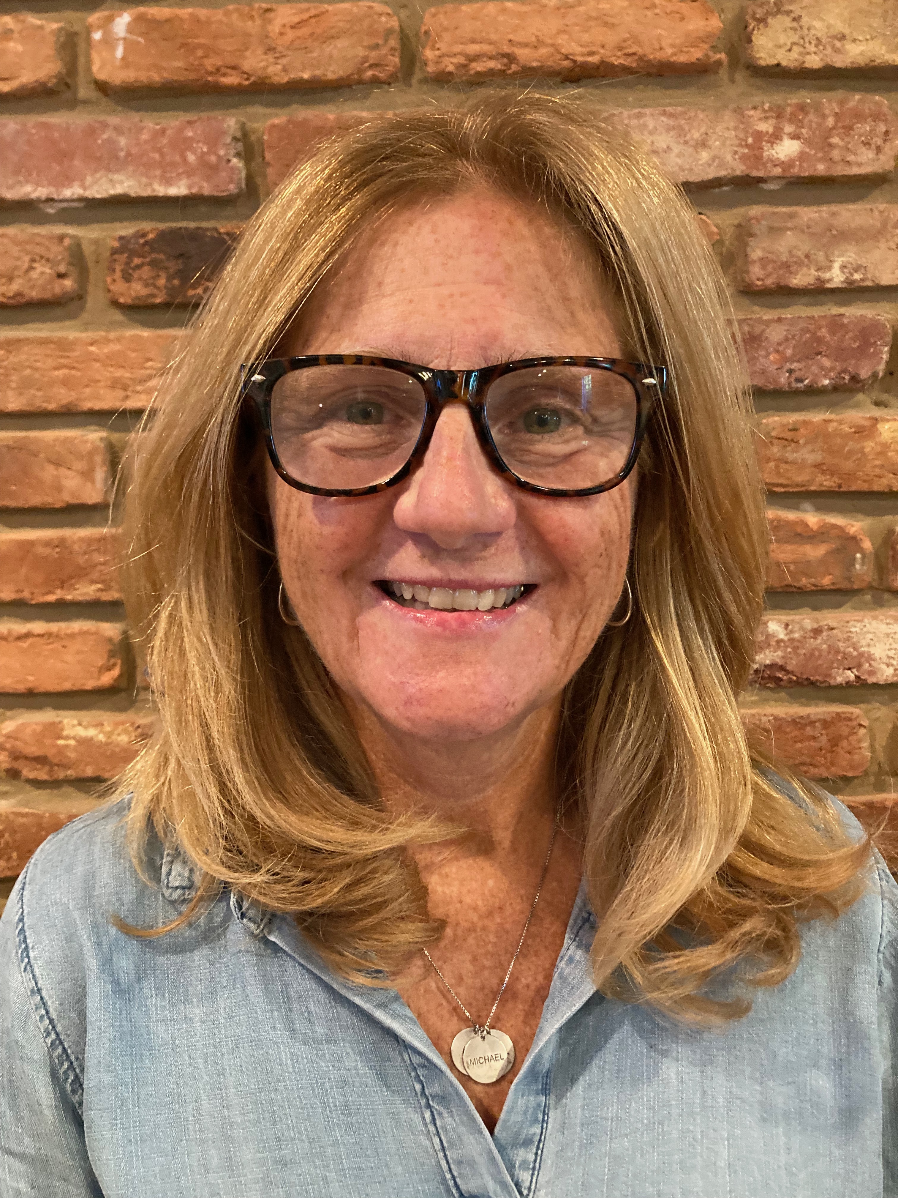 ann wears glasses and is in front of a brick wall