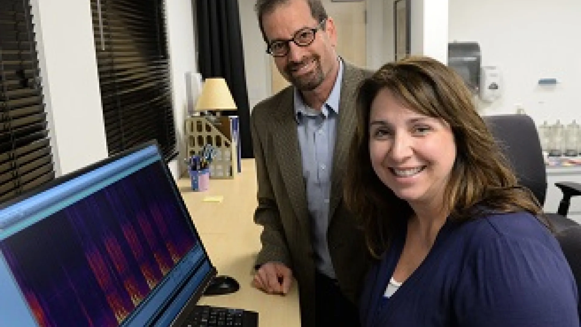  Dr. Jordan Green and Dr. Tiffany Hogan standing in front of a computer monitor, smiling at the camera.
