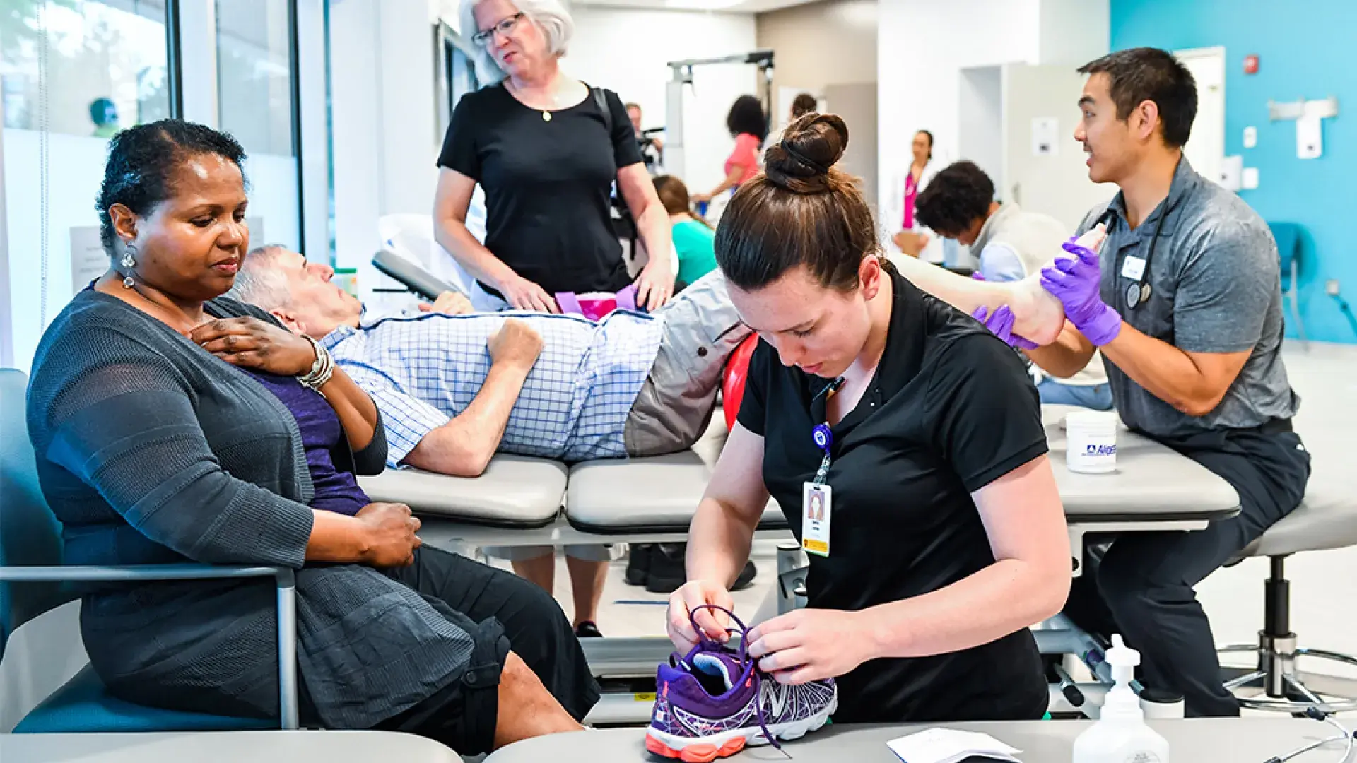 PT students work with patients, one ties a shoe the other rubs a foot