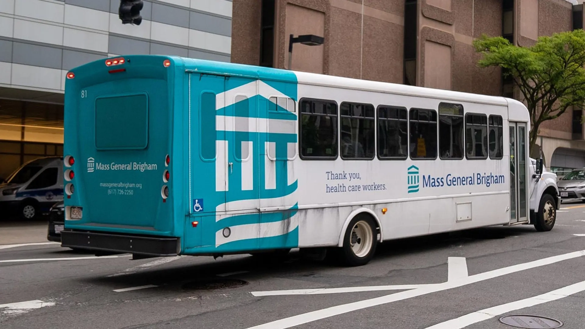 a teal and white Mass General Brigham bus drives on the road