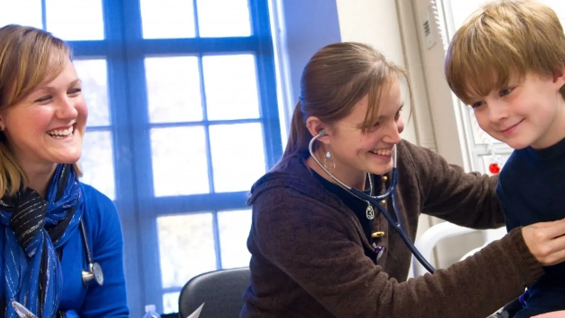woman uses stethoscope on a boy while another smiles