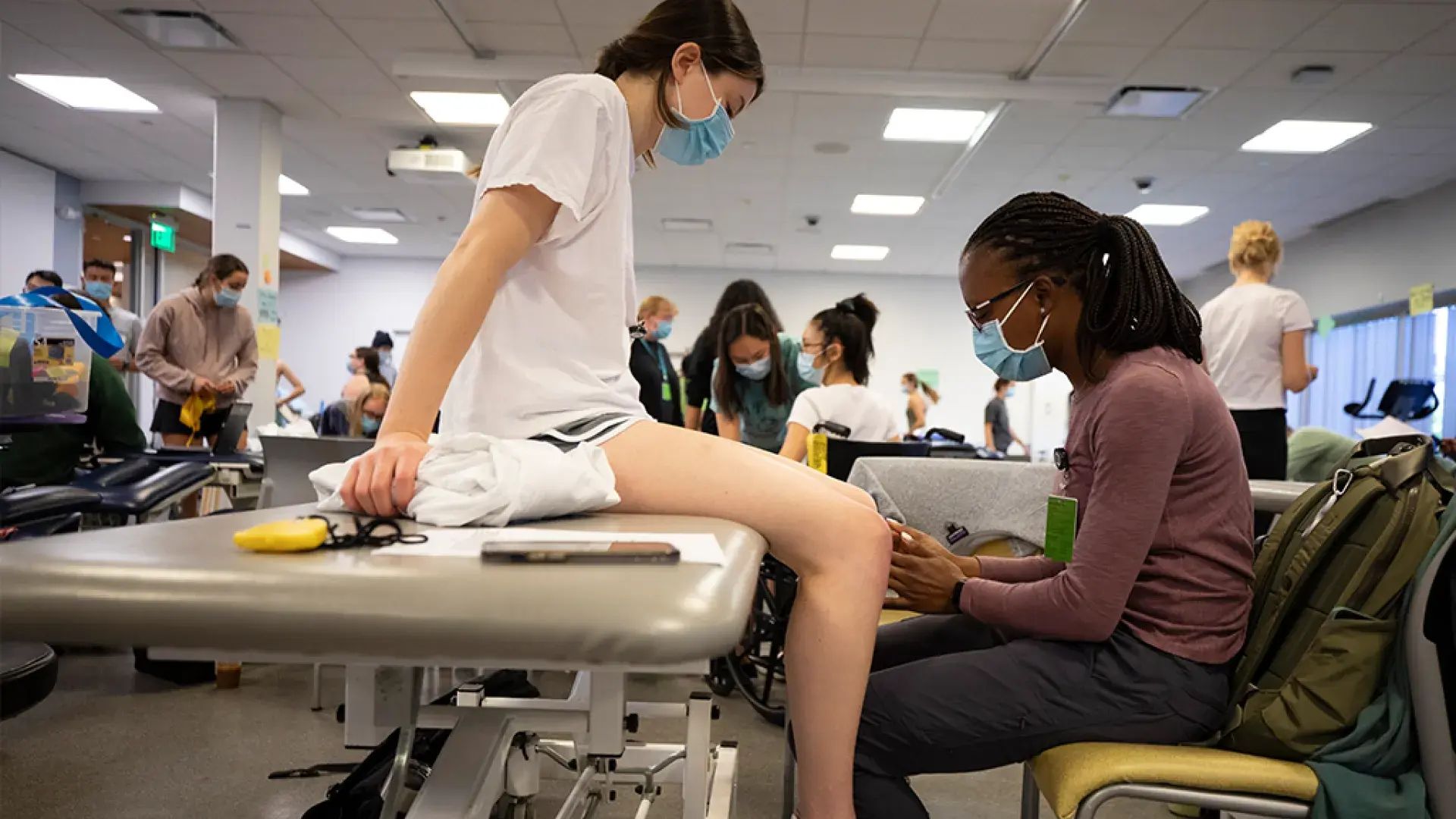 students in mask work together one on an exam table the other touching her knee