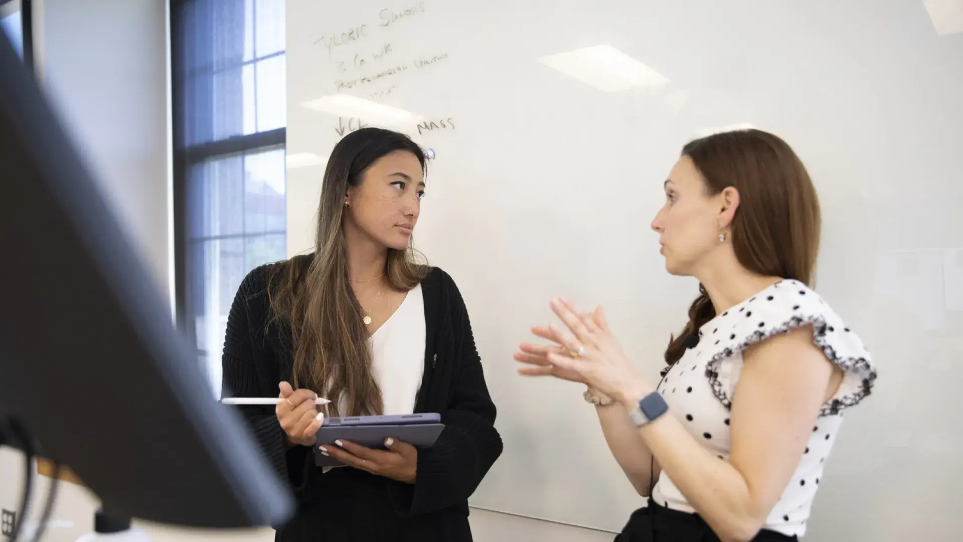 Professor gestures to a student in front of a white board