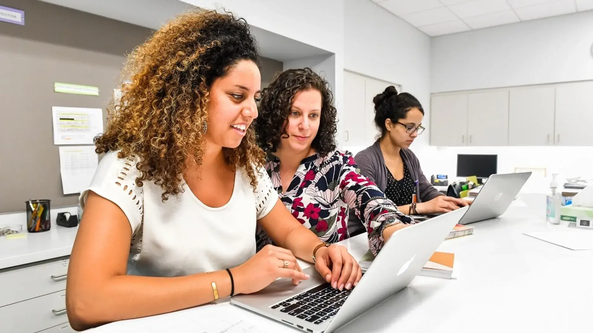woman looks over shoulder of student at laptop