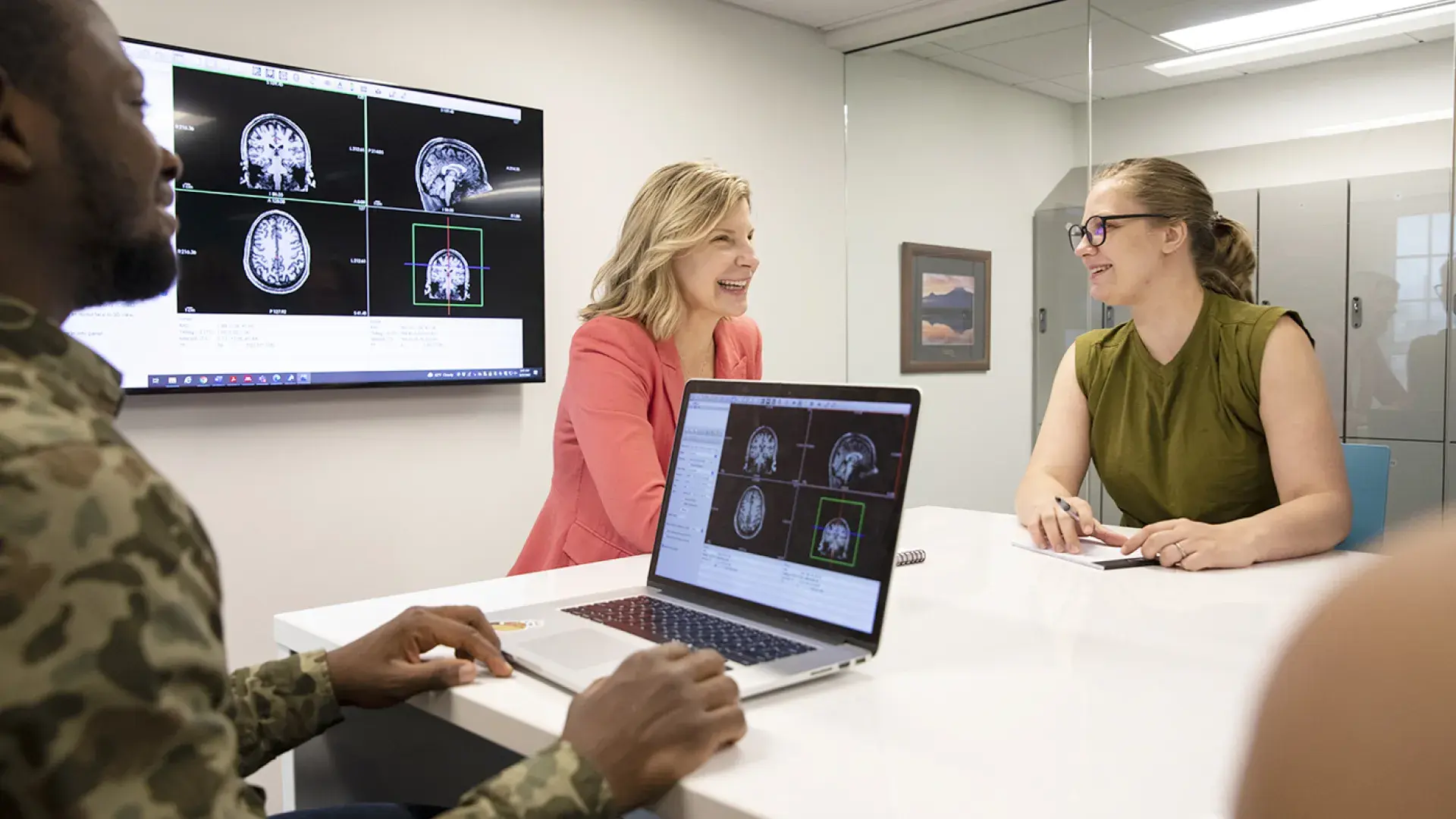 two women and a man converse and look at brain scans on screens