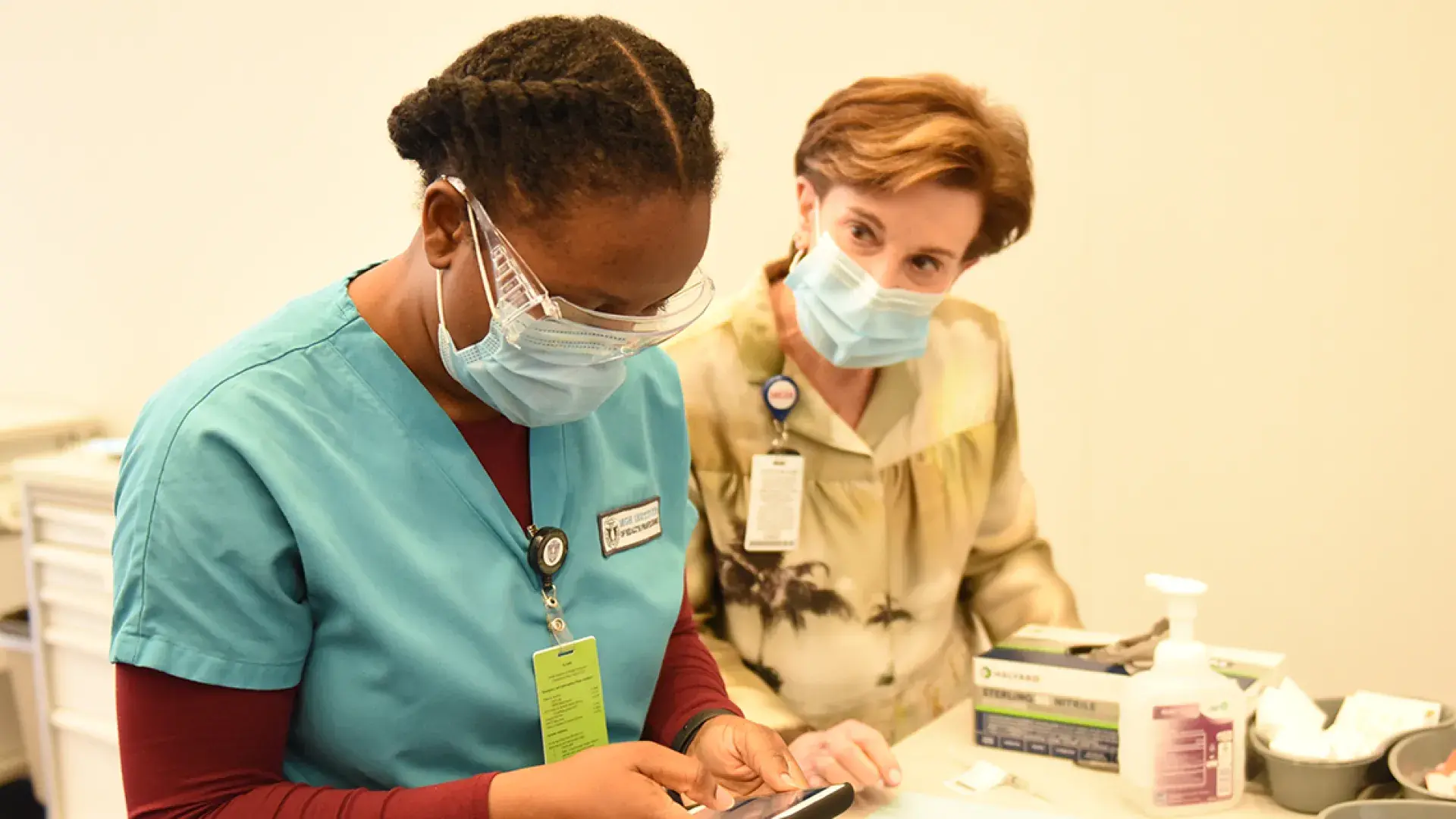 Photo of woman talking with student in scrubs, both wear masks
