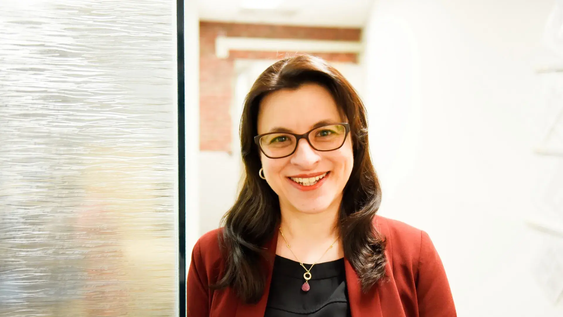 profile photo of Joanna wearing a red cardigan and glasses leaning against a glass wall and smiling