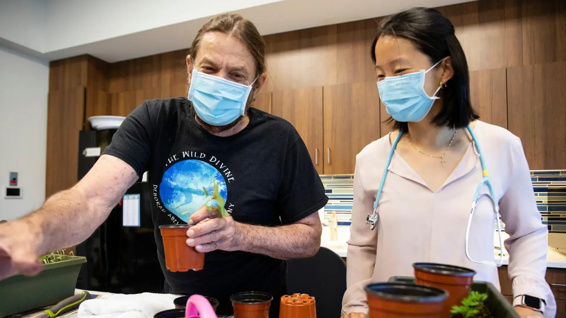 a woman in a stethoscope looks on while an older man plants a plant