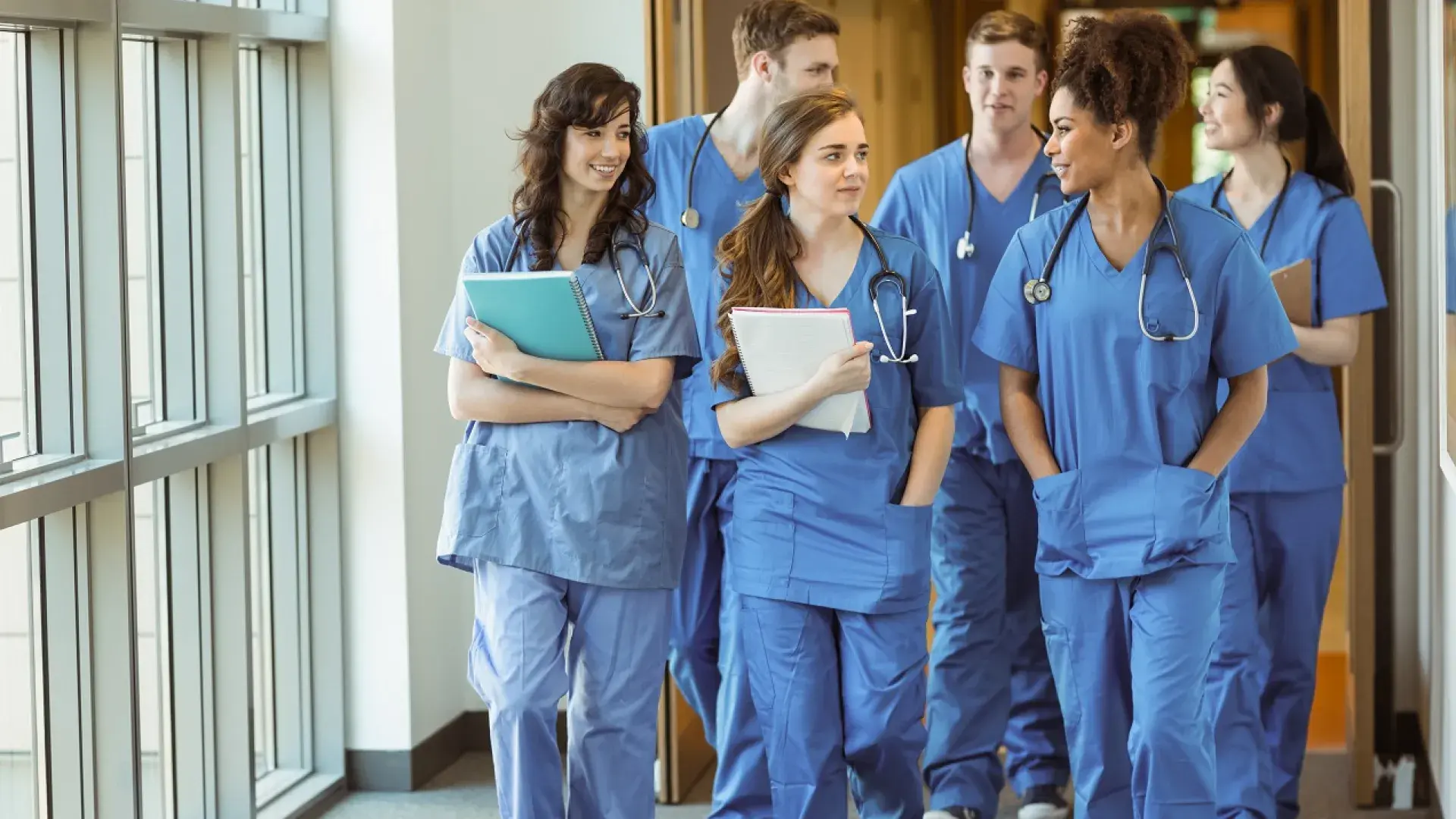 a group of people walk down a hallway in scrubs