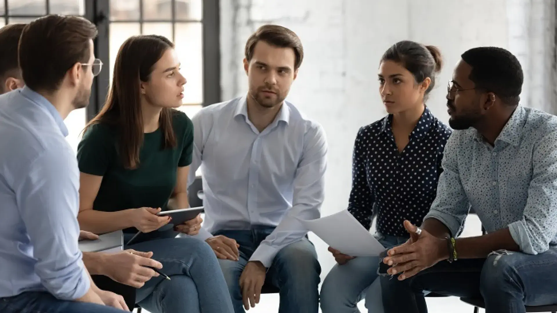 group of people with stern faces speak in a circle to each other