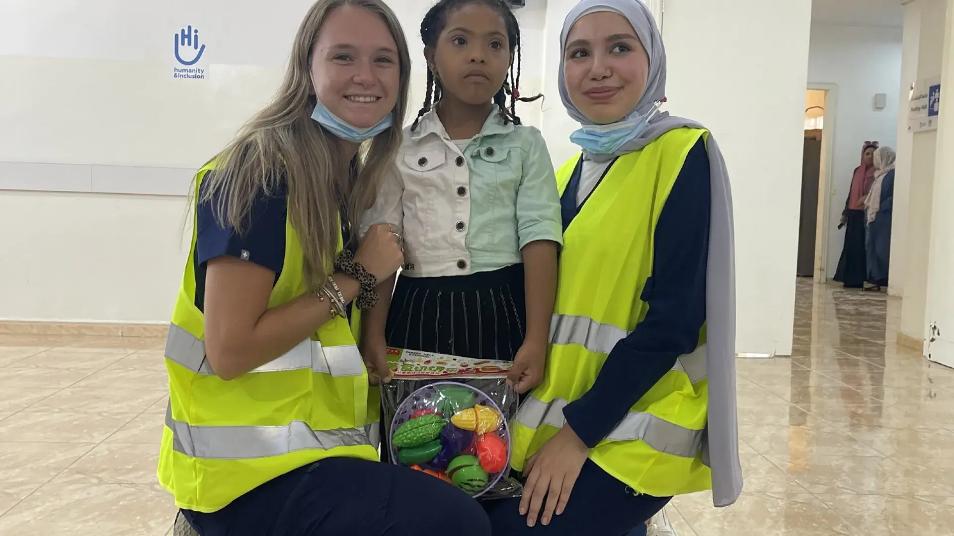 two women in yellow vests squat next to a jordanian child