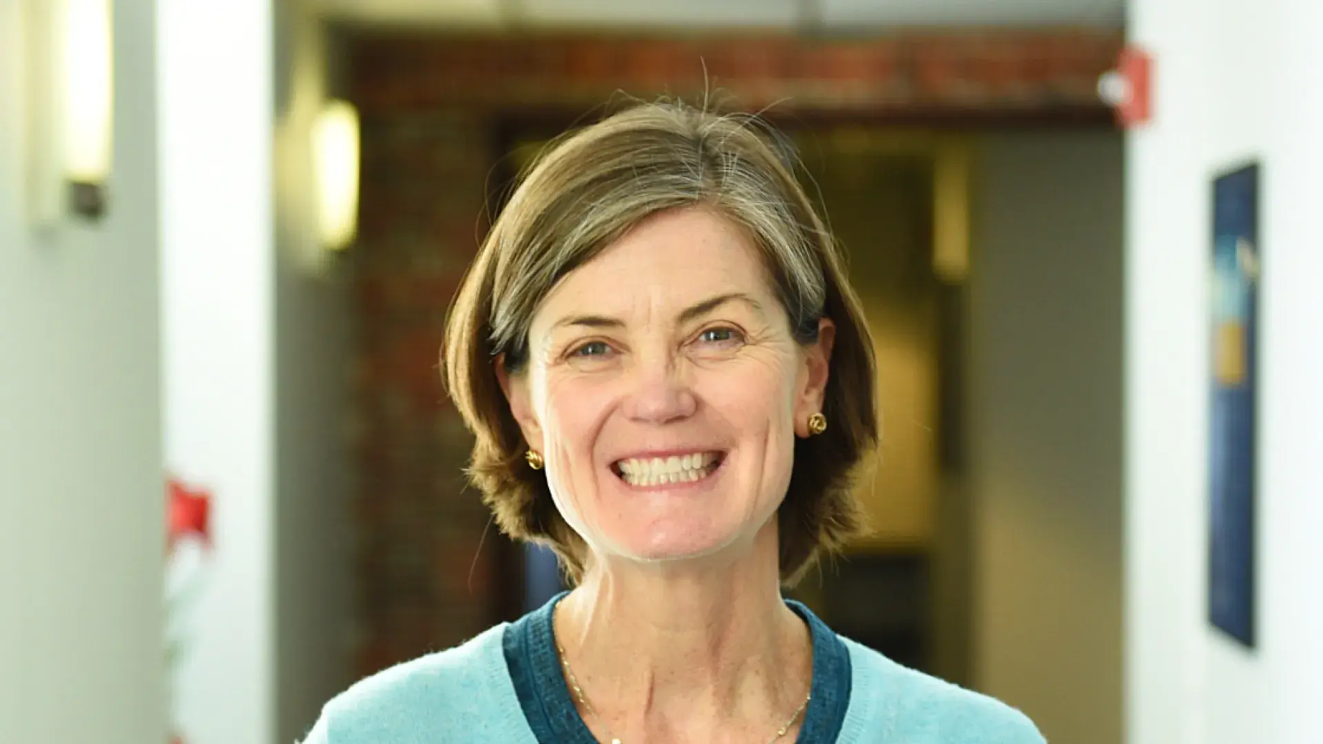 betsy cox wears a teal colored v neck sweater and has short brown hair