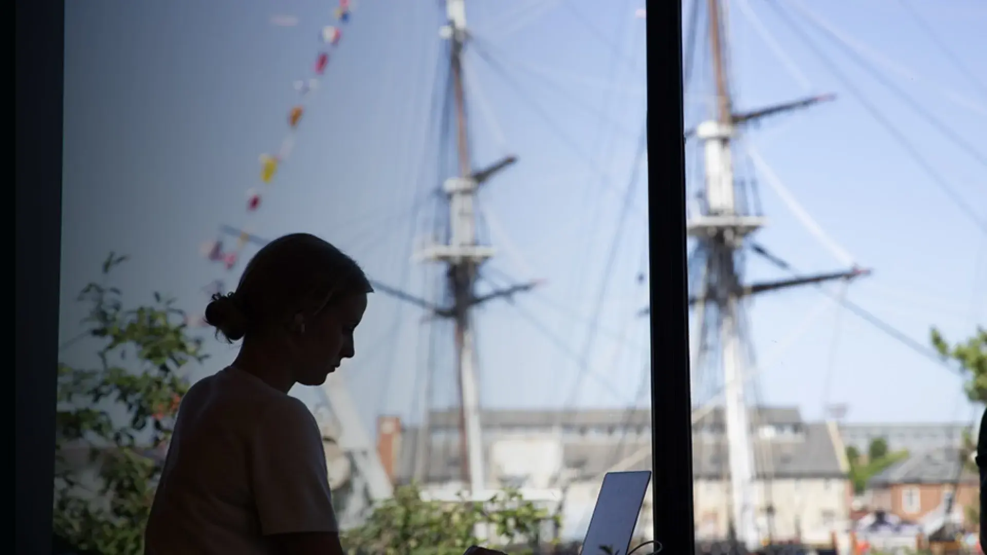 woman sits at laptop with ship mast in the background