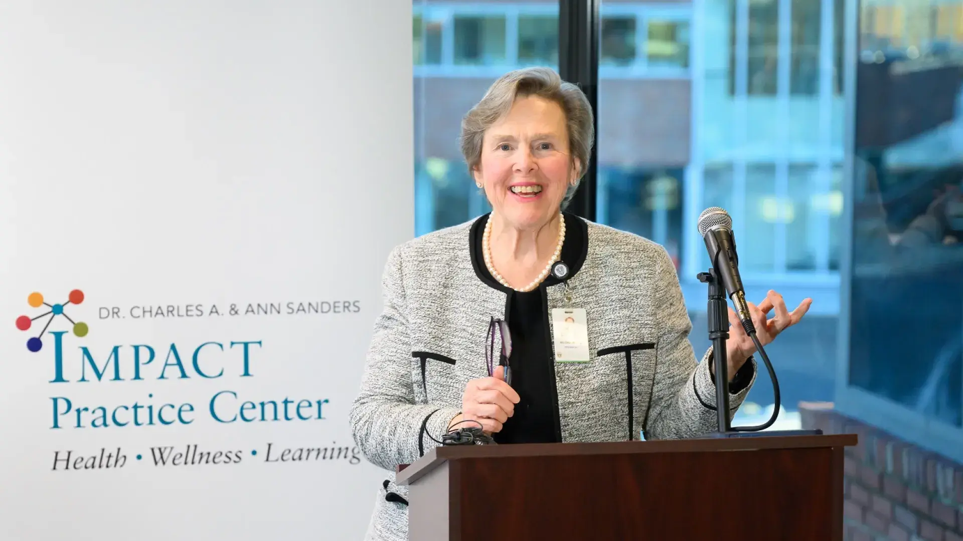 paula wears a grey suit and gestures at a podium