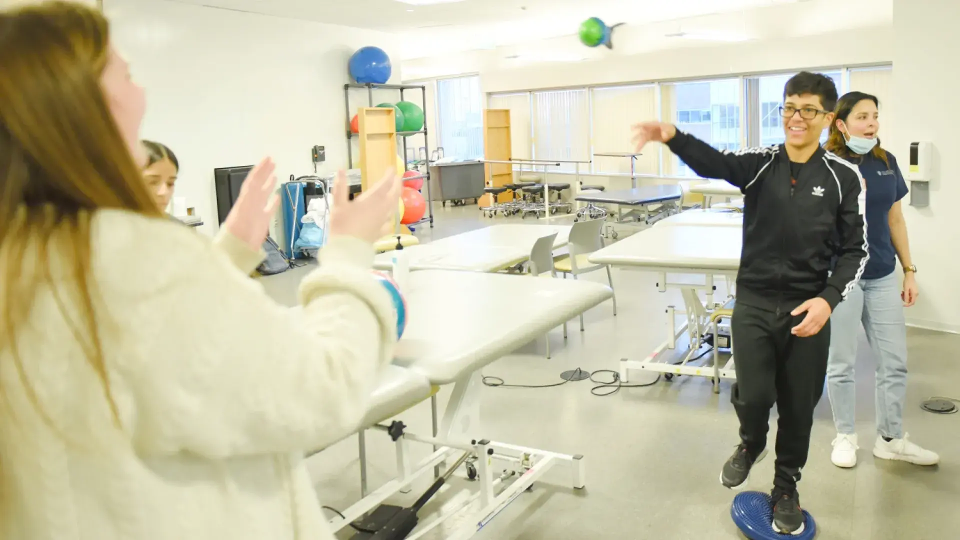 person balancing on a squishy blue disk throws a ball to a person with waiting open arms