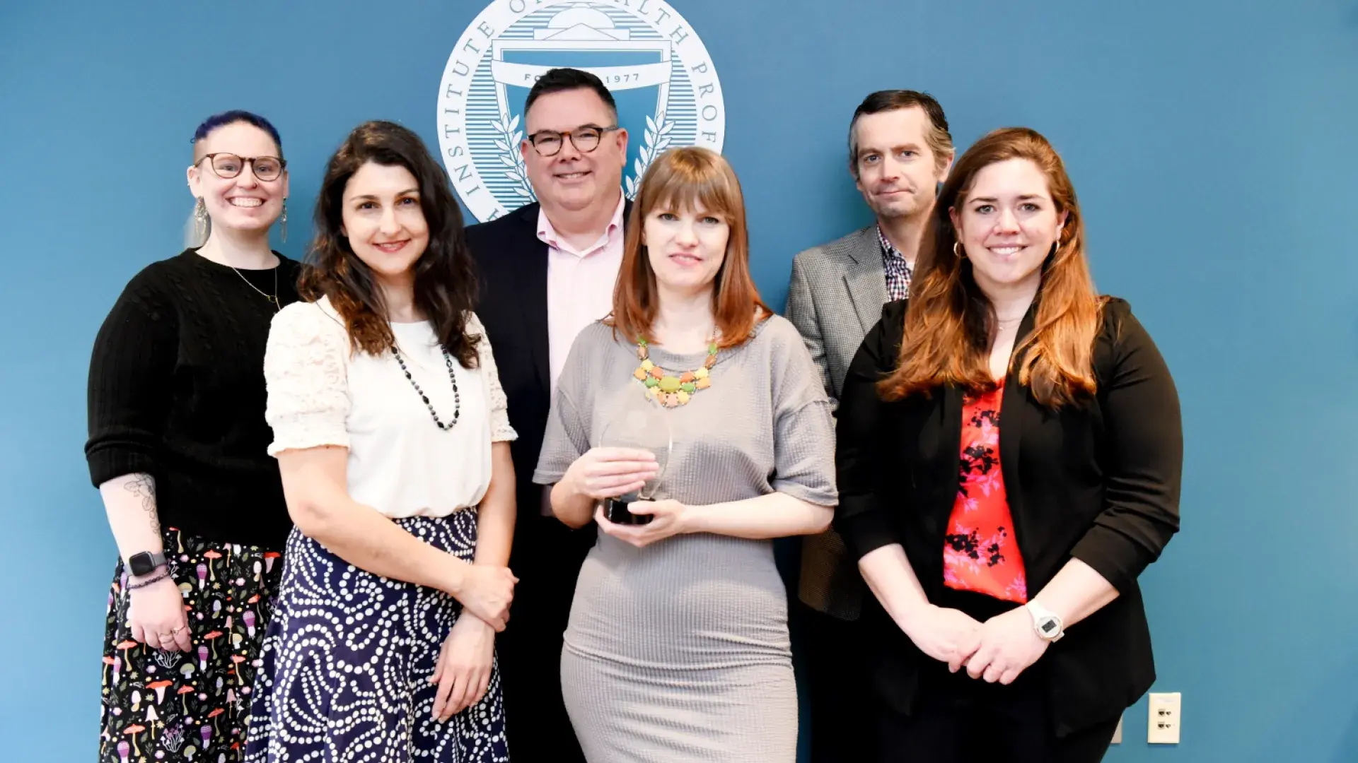 group of people smile, woman in front holds tear-drop shaped glass award