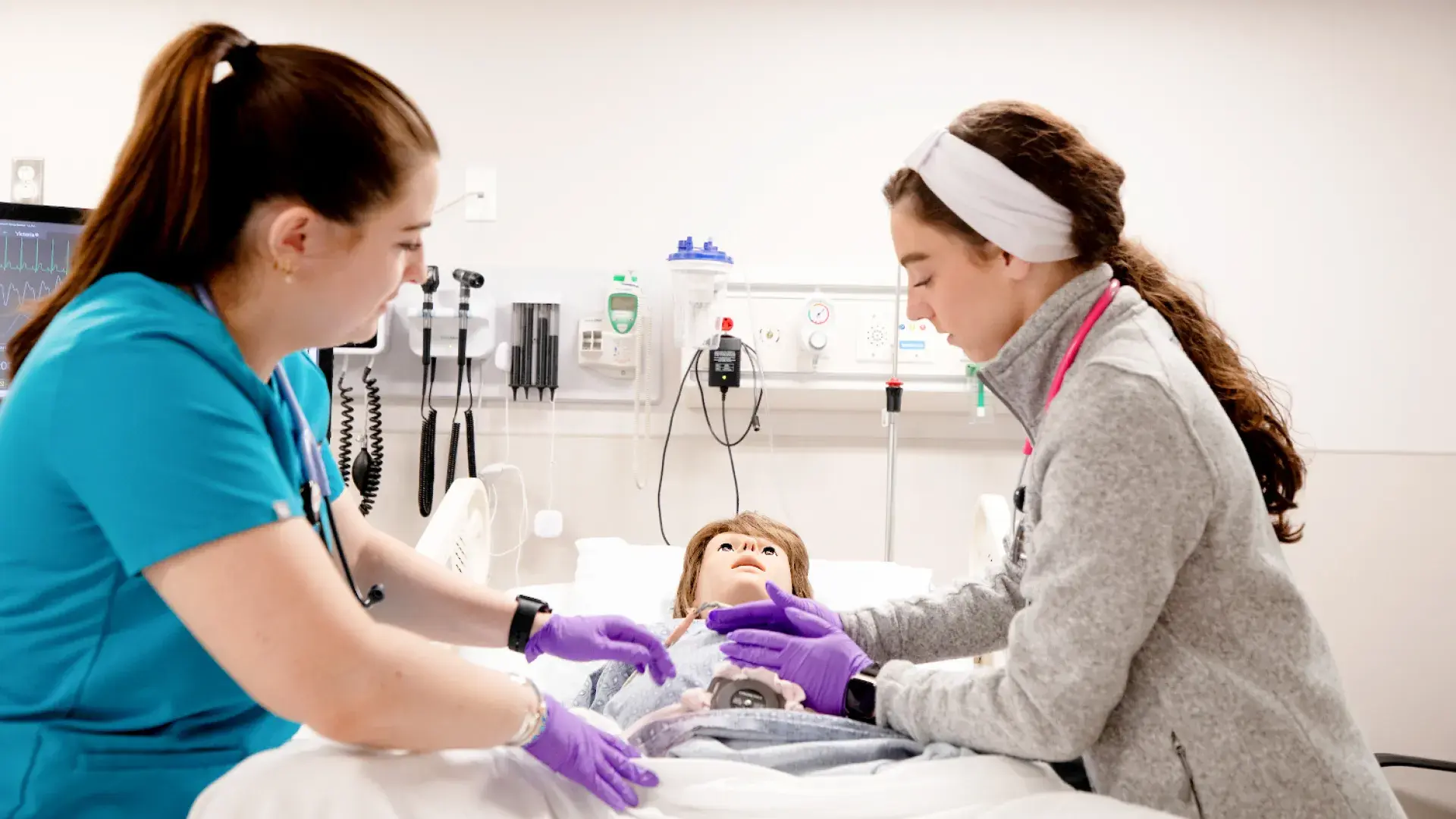 Two nursing students working with a simulation manikin in-between them..