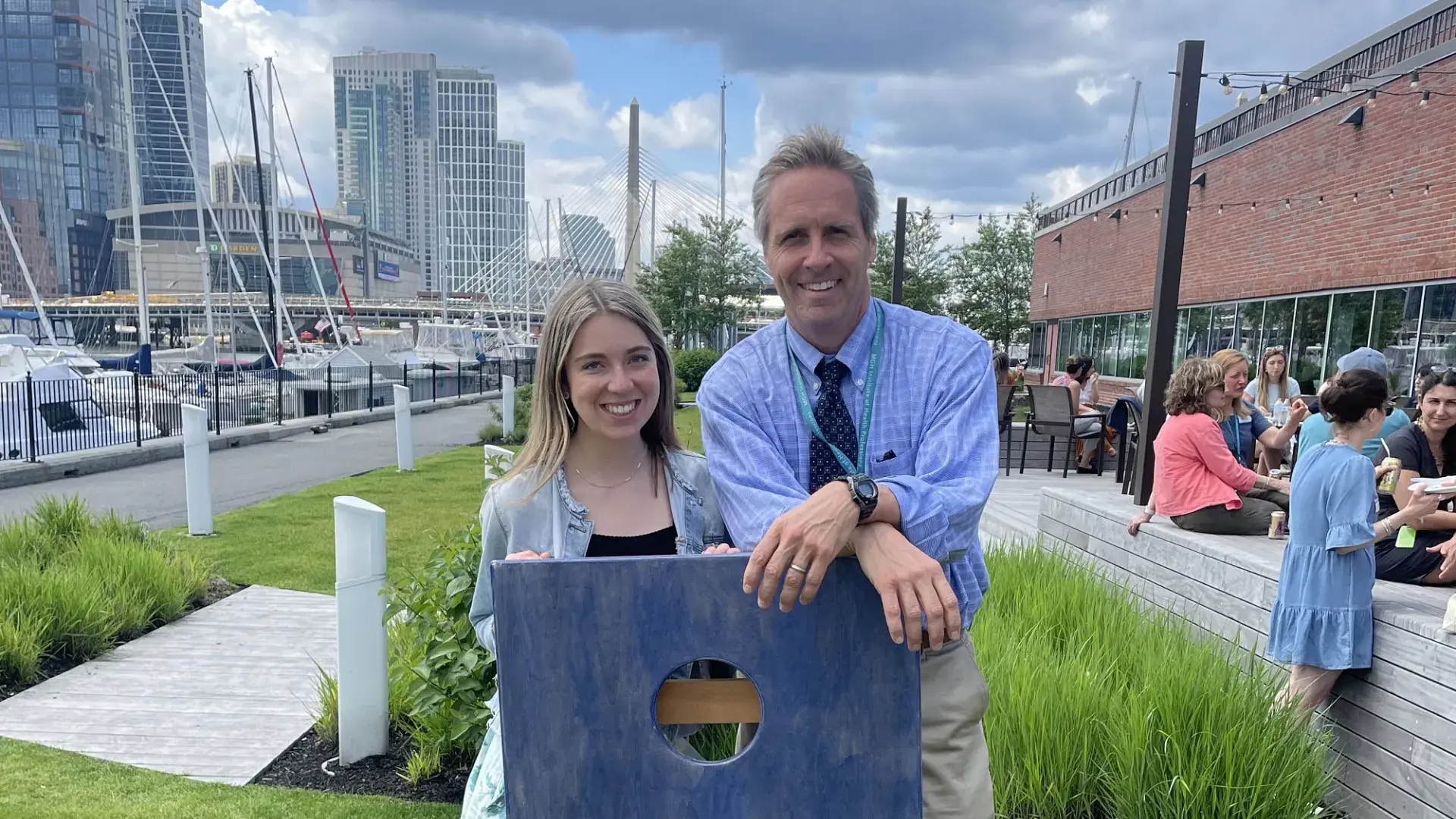 sean and riley pose with a cornhole board in front of the boston skyline