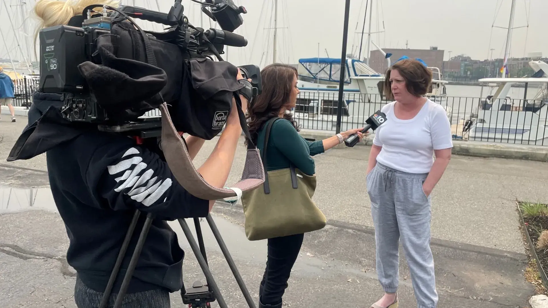 news crew with microphone and camera stand and speak to sue who wears a white top and grey pants