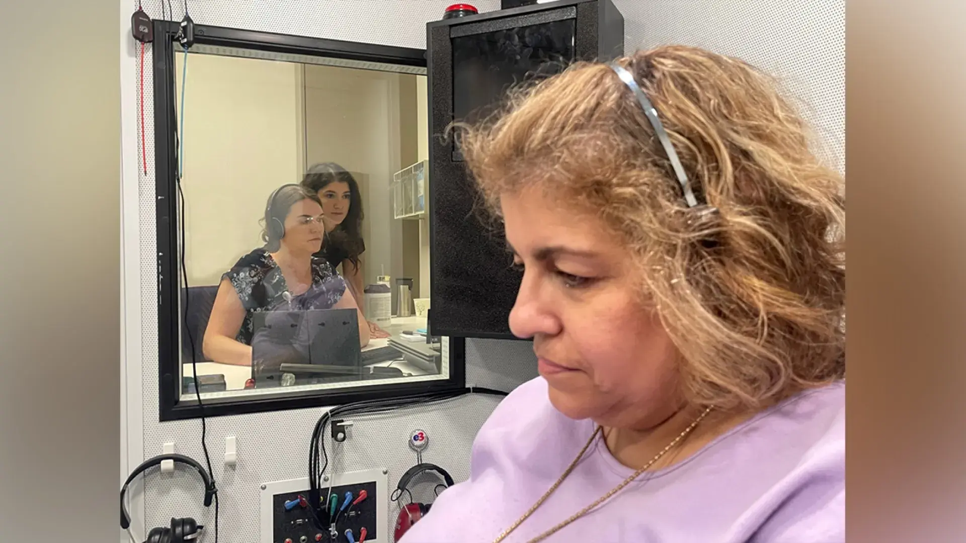 Woman with headphones in room with two people observing through a window