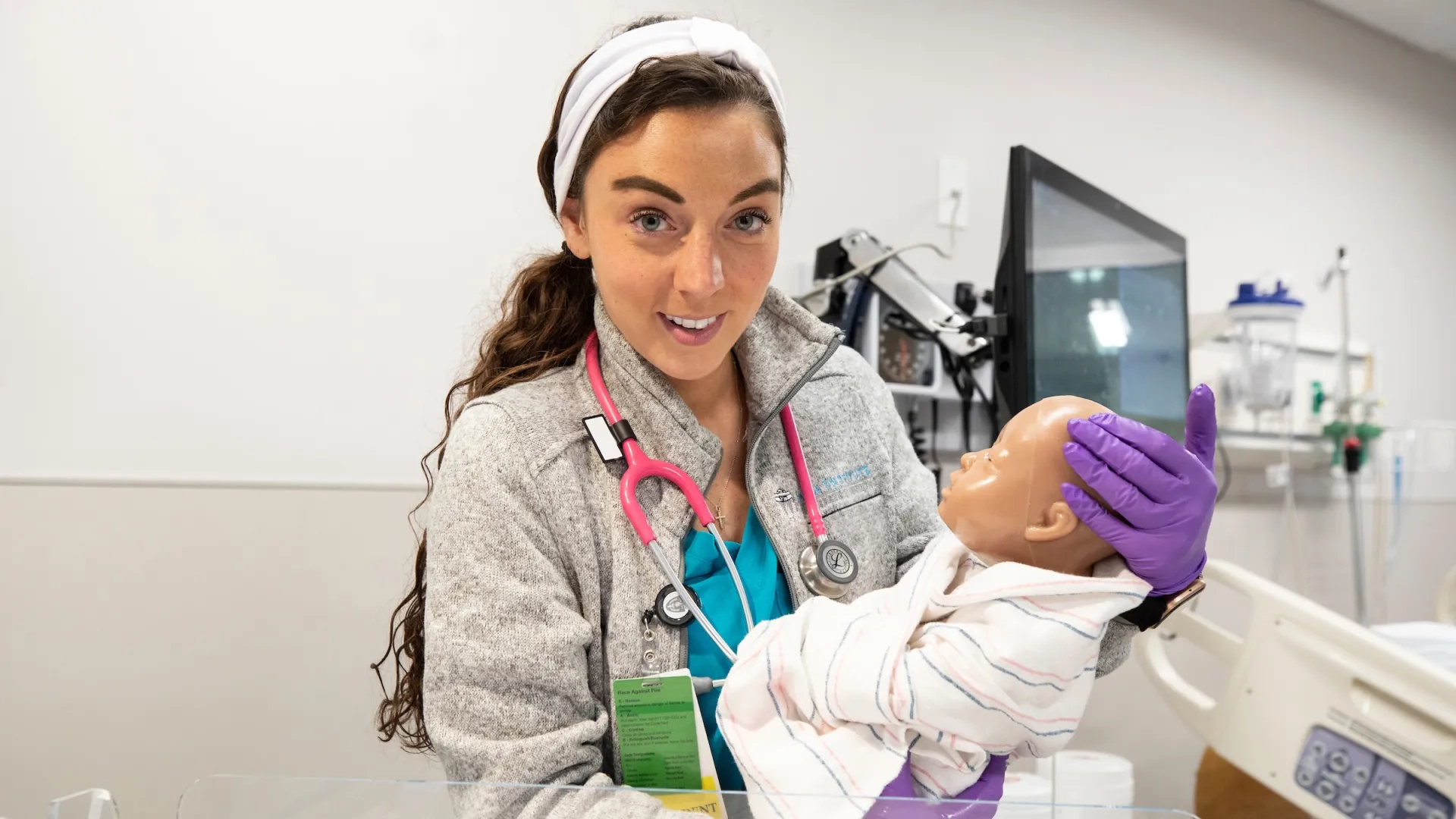 A student in the Fast-Track BSN Program holding an infant mannequin during a hands-on nursing licensure preparation session. The student is dressed in scrubs and is actively participating in the accelerated nursing curriculum, which is part of an intensive nursing training program designed for professionals transitioning to nursing careers.