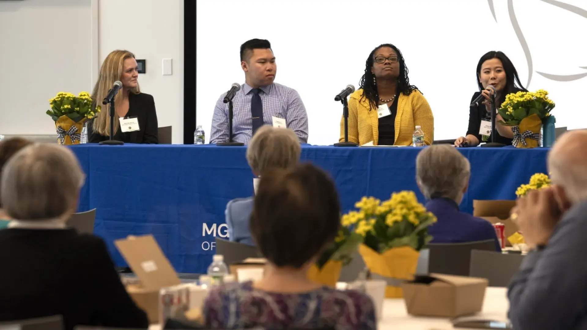 4 people sitting at table, while one talks