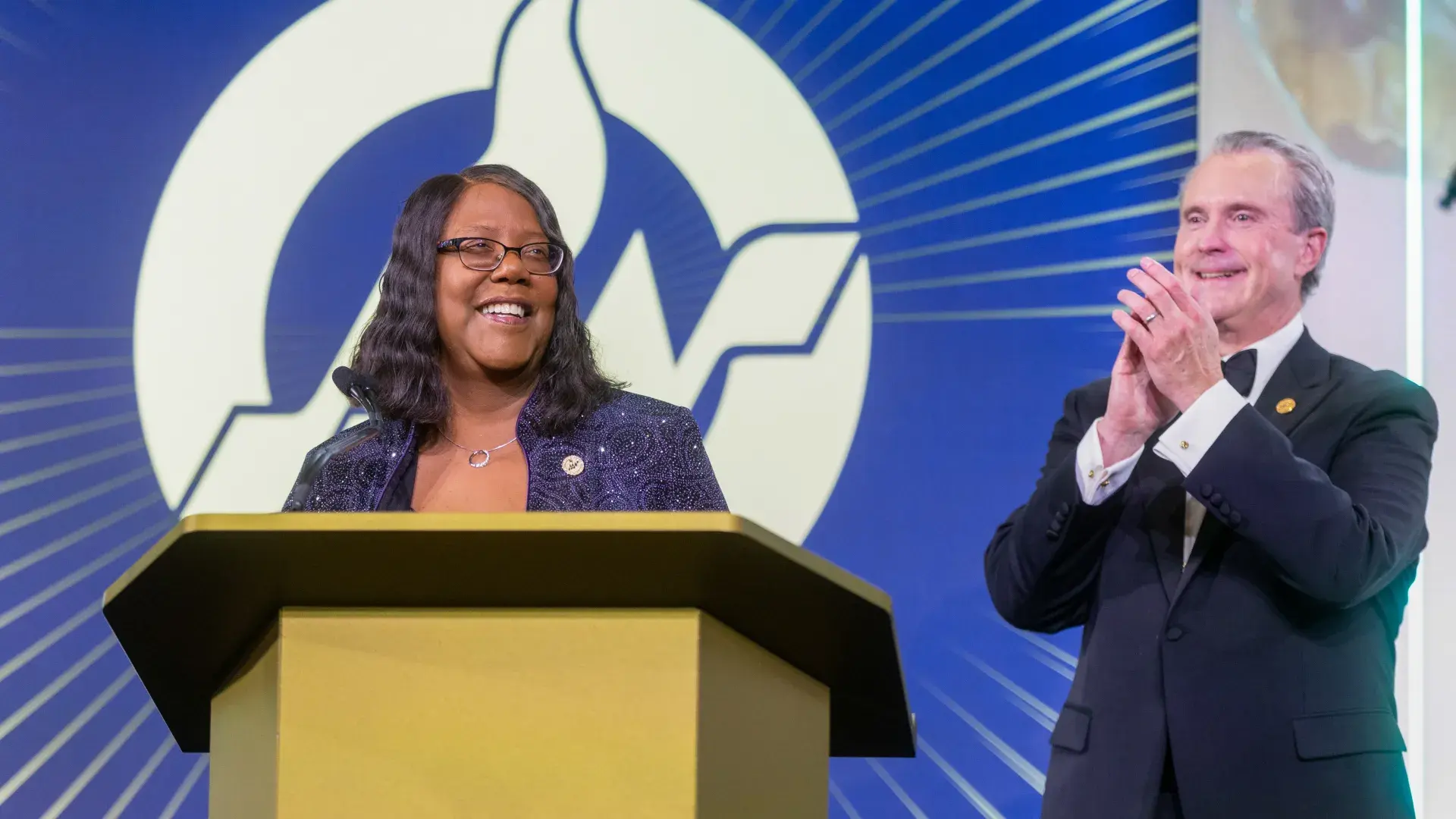 Man claps next to woman at podium