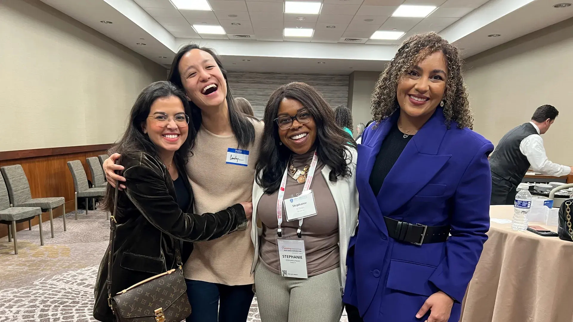 four women stand close and smile