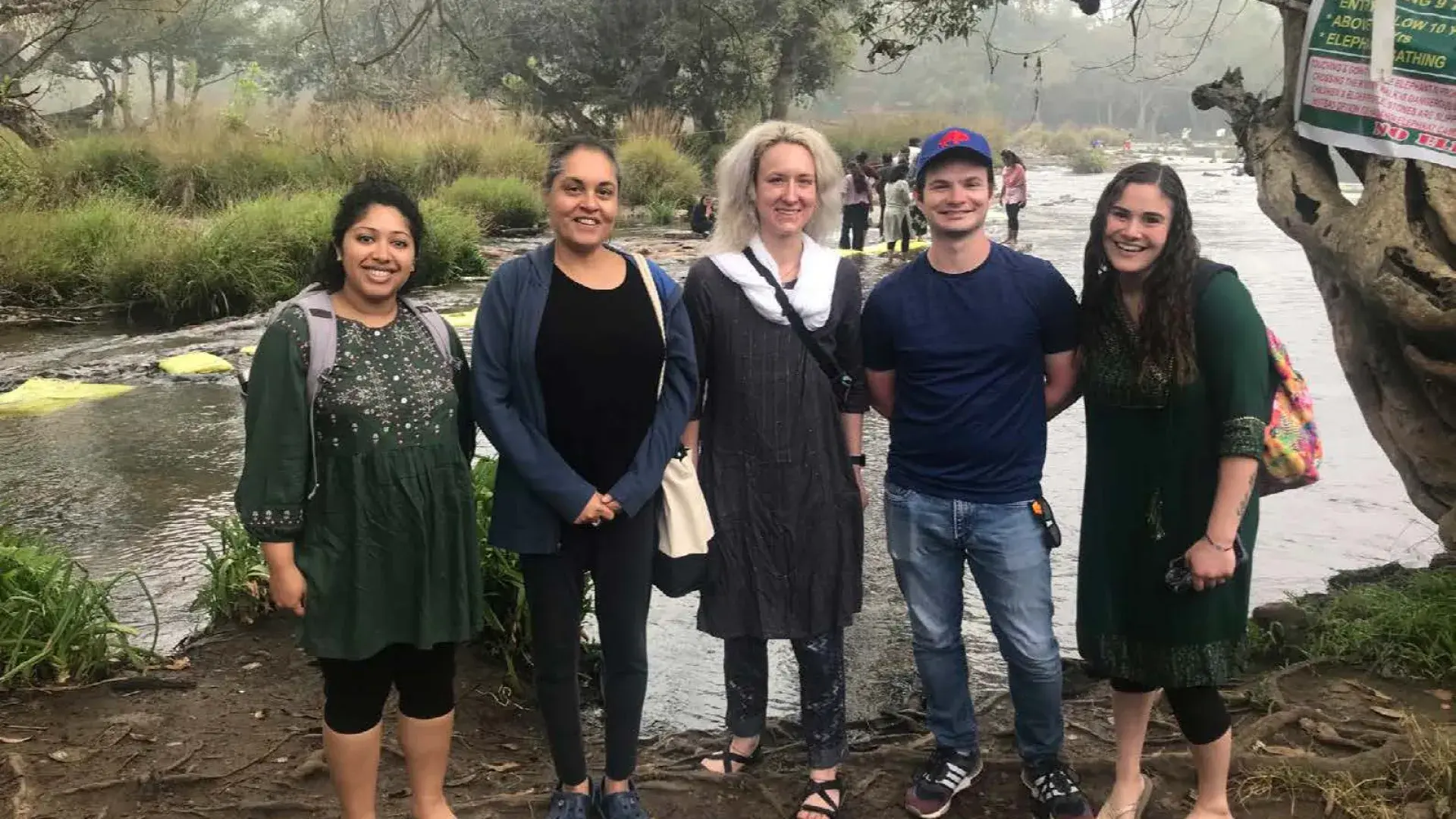five people pose and smile on the bank of a river